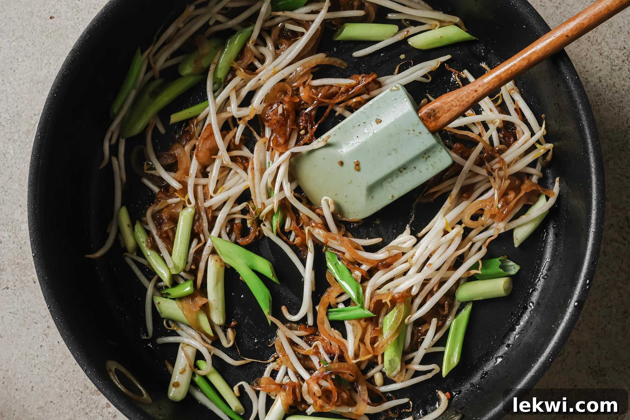 Bean sprouts, green onion and garlic cooking in a large pan.