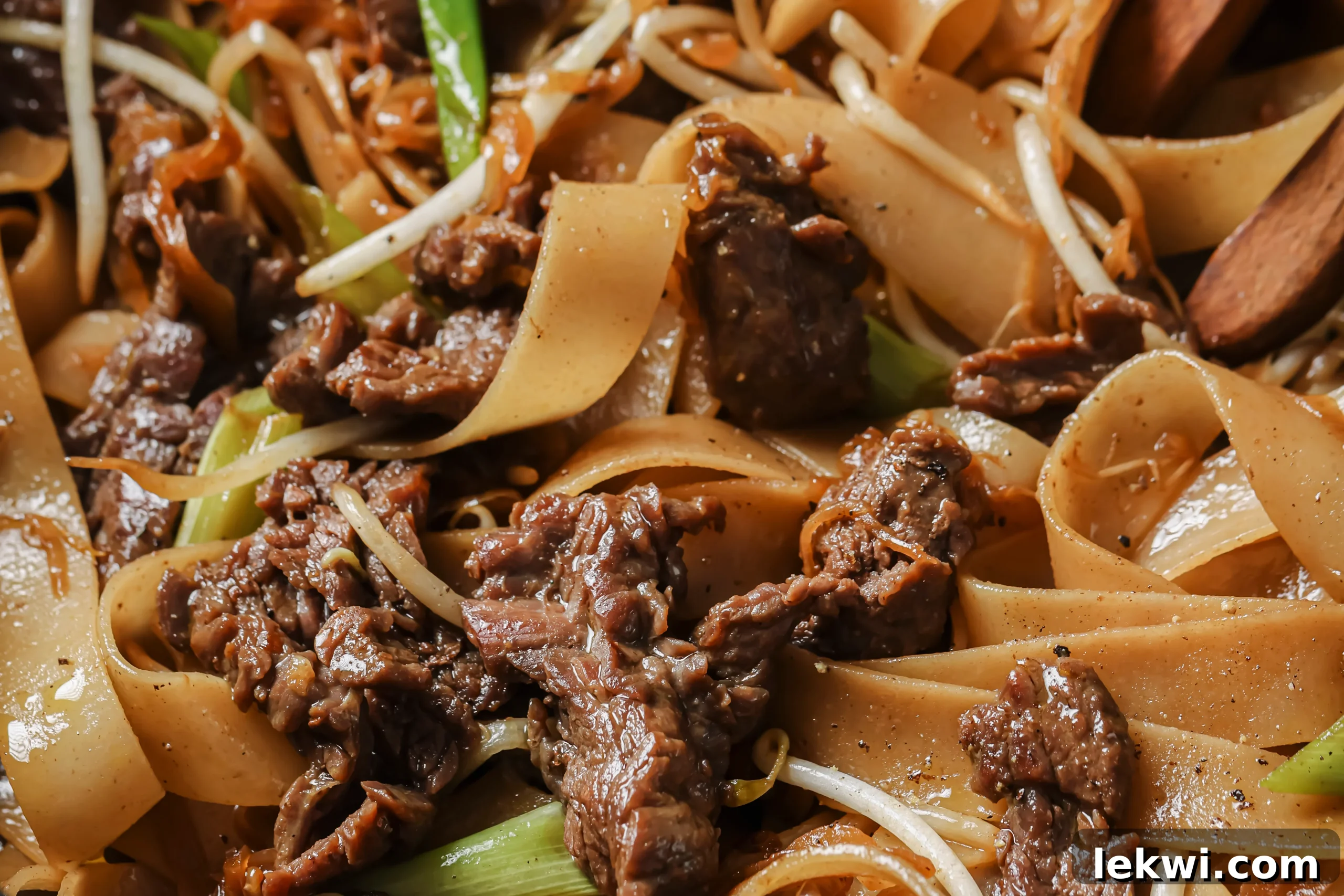 Cooked beef chow fun with noodles and veggies close up in a large pan.