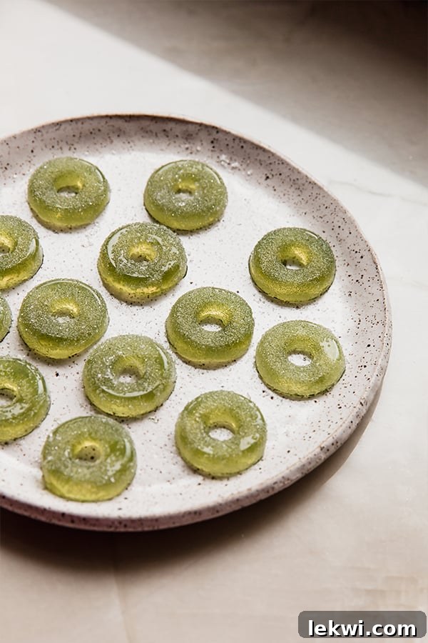 A full plate overflowing with vibrant, perfectly set homemade sour apple ring gummies, showcasing their inviting texture and natural green color.
