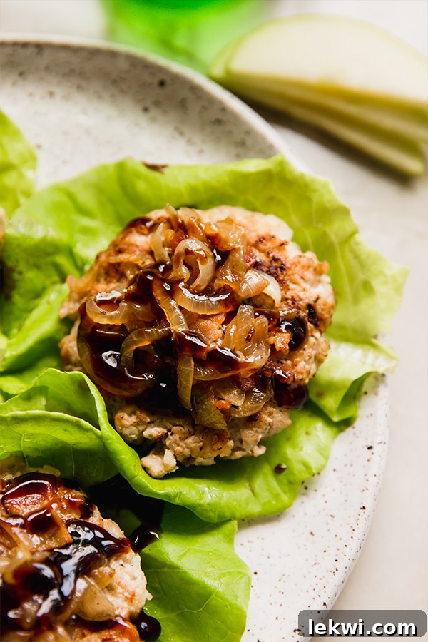 A plate featuring several apple chicken burgers served in crisp lettuce wraps, garnished with fresh herbs.