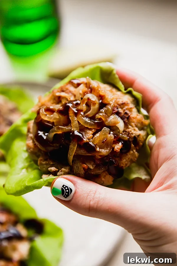 A person holding a perfectly cooked apple chicken burger nestled in lettuce, ready to be enjoyed.