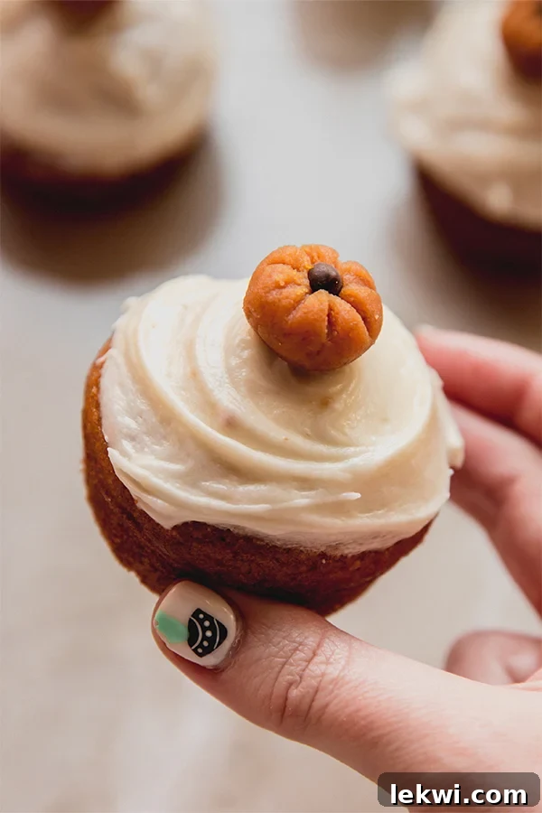 Person holding a pumpkin spice cupcake topped with a decorative pumpkin.