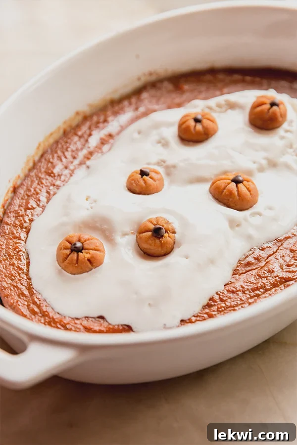 Pumpkin pudding in a baking dish topped with whipped coconut cream and mini pumpkin buckeyes, ready to serve.