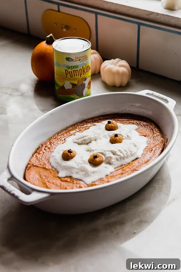 A finished baked pumpkin pudding, golden brown and creamy, resting on a counter with decorative canned pumpkin and mini pumpkins in the background.