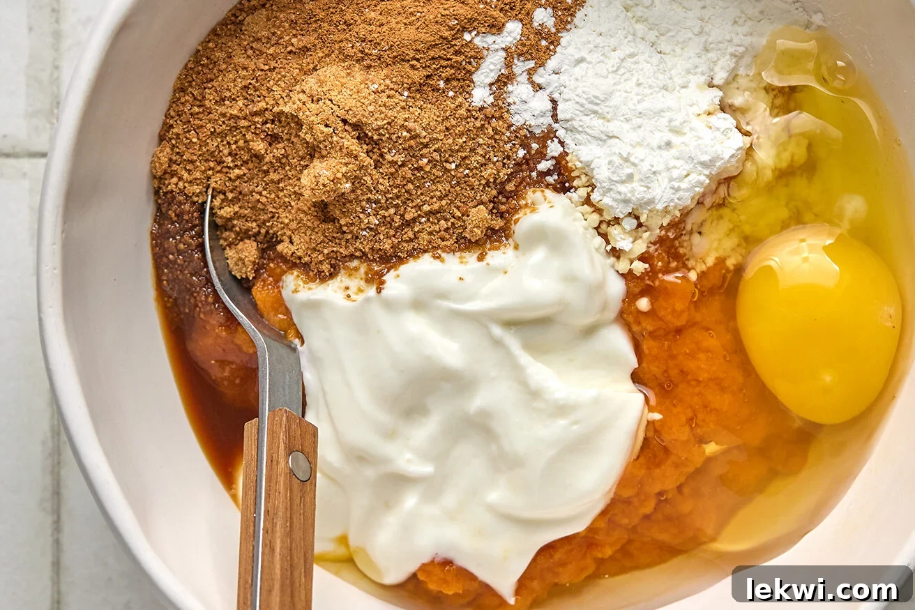 Ingredients for the pumpkin pie layer, including pumpkin puree, coconut yogurt, and spices, unmixed in a bowl.