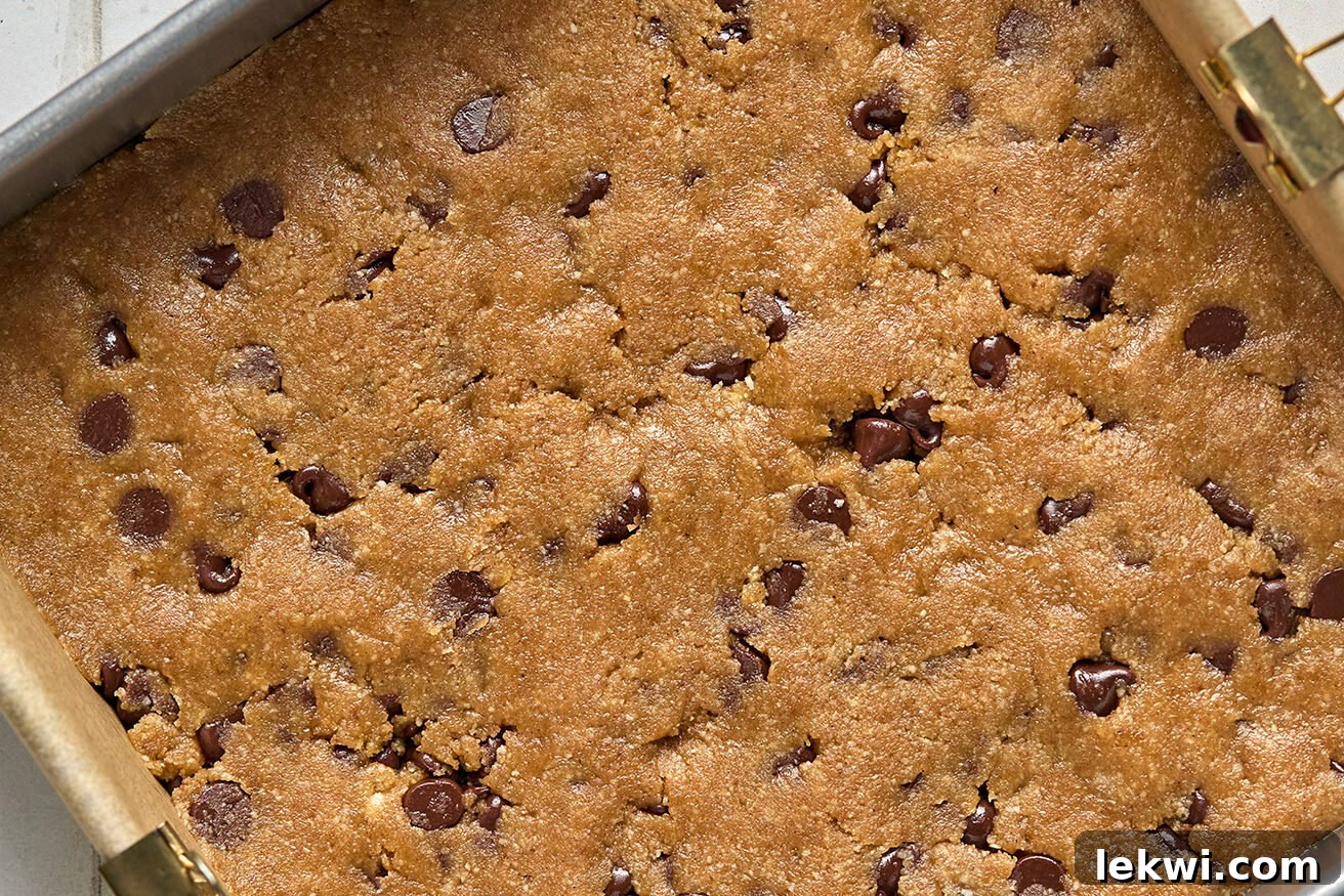 The chocolate chip cookie dough evenly pressed into the bottom of an 8x8 inch baking pan, forming the base for the pumpkin bars.