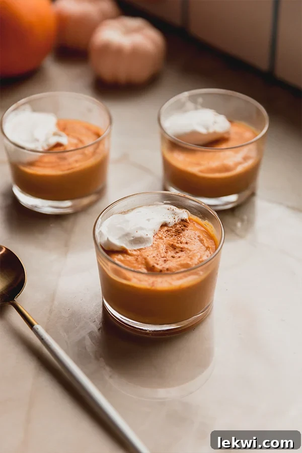 Small pumpkin cream cups with a spoon, garnished with whipped coconut cream and cinnamon.