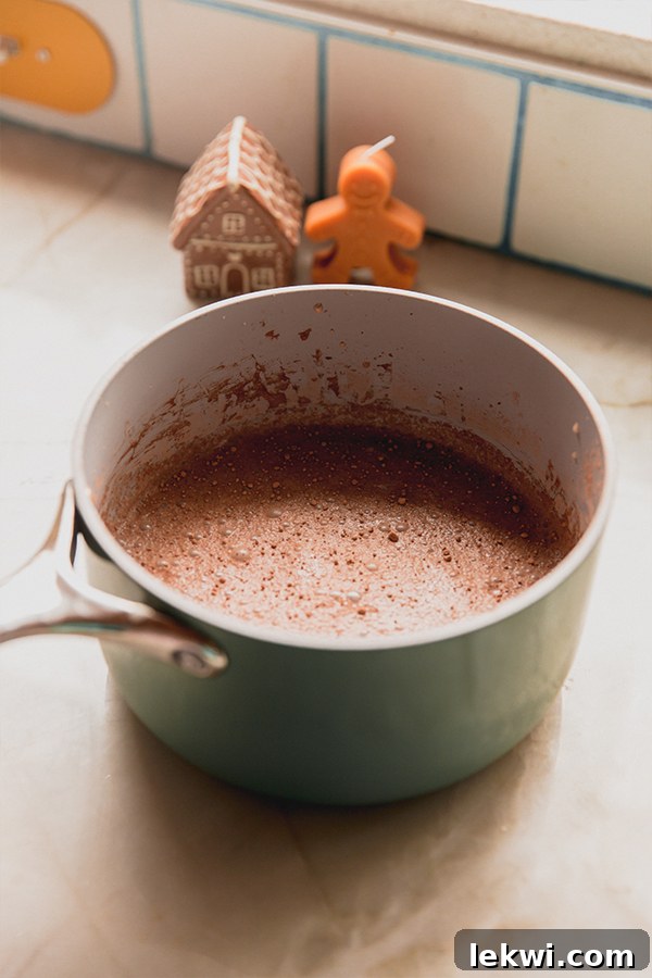 A pot of gingerbread hot cocoa steaming on a stove, ready to be poured into mugs, showing its rich, dark brown color.