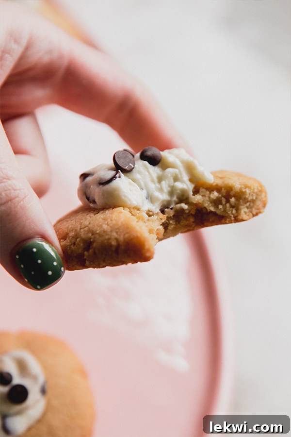 A cannoli thumbprint cookies being held in a hand with a bite taken out of it.