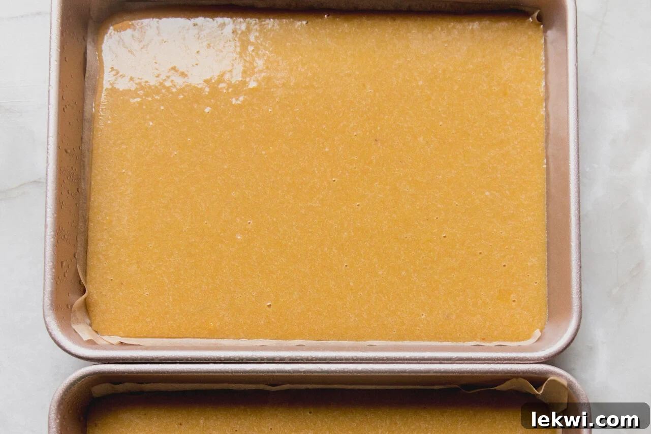 Dividing the prepared Christmas tree cake batter evenly into two baking pans.