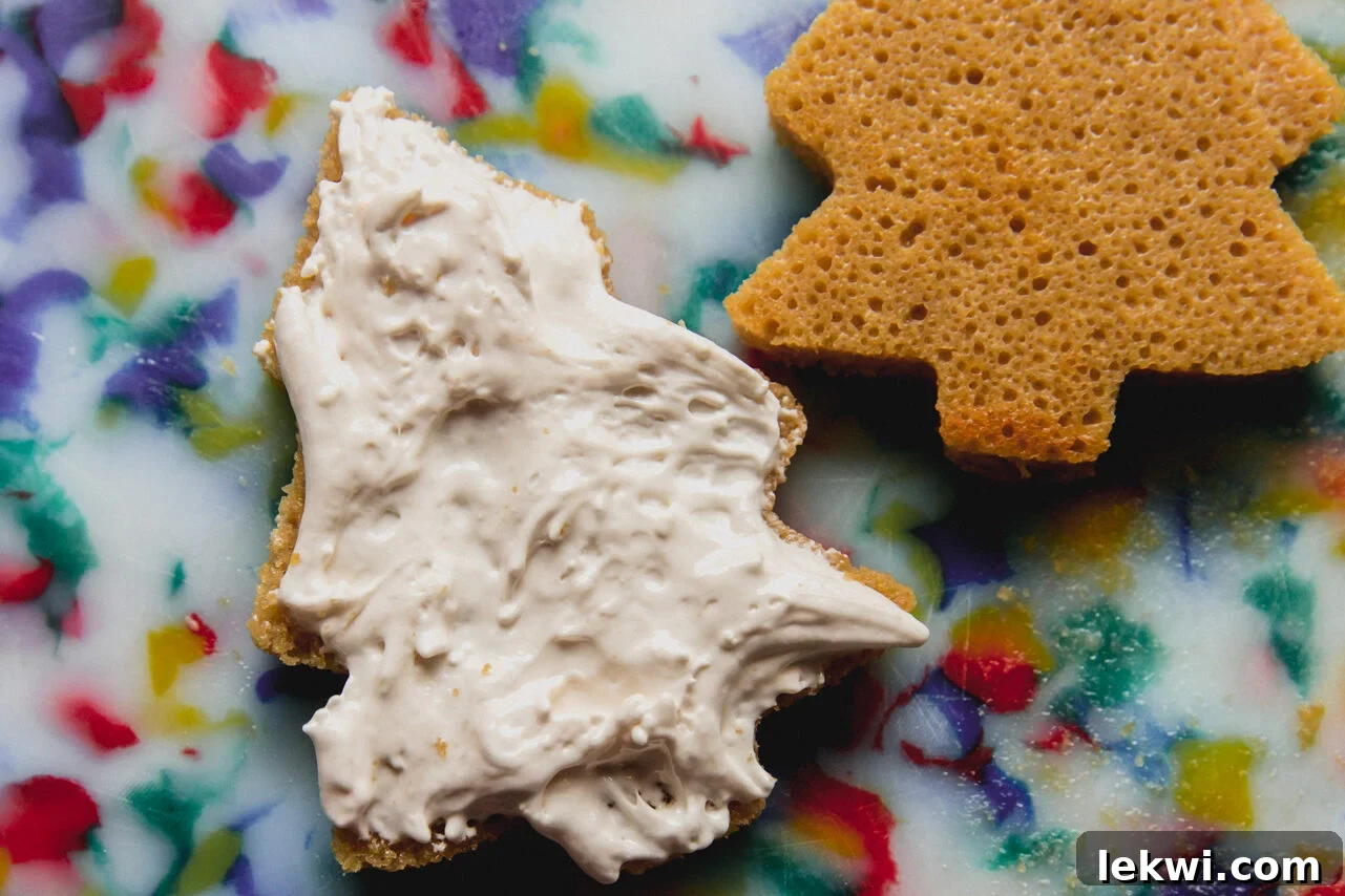 Assembling Christmas tree cakes by spreading marshmallow cream between two cake cutouts.