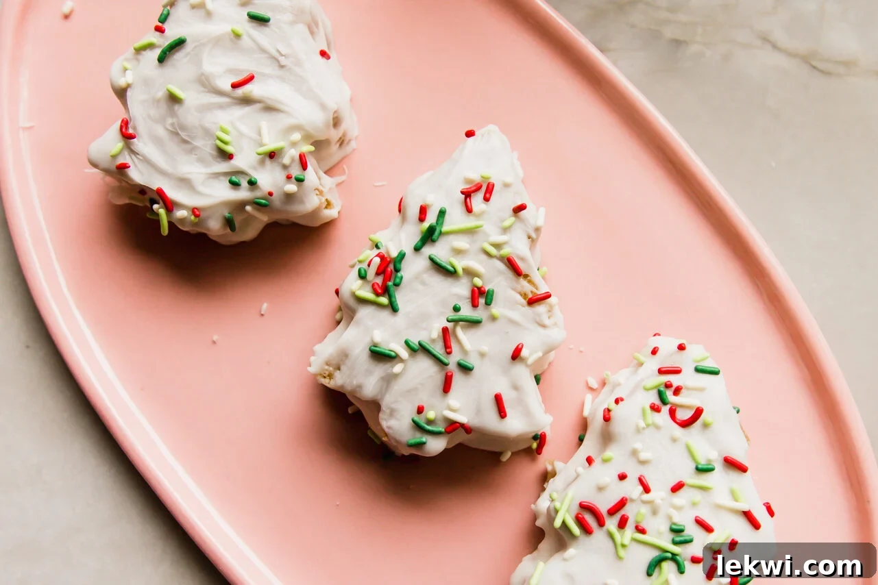 Three fully decorated Christmas tree cakes with white chocolate coating and sprinkles, arranged on a pink plate.