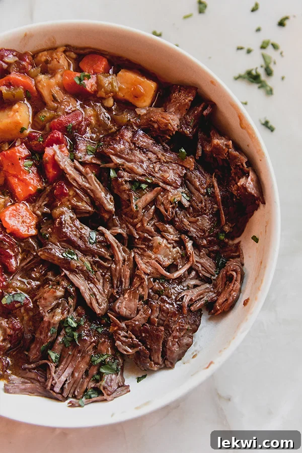 A beautifully presented bowl of Italian pot roast, garnished with fresh herbs and vibrant roasted vegetables.
