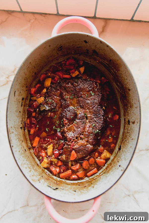 A large, rustic Dutch oven filled with Italian pot roast, showcasing the rich sauce and tender ingredients, ready for the oven.