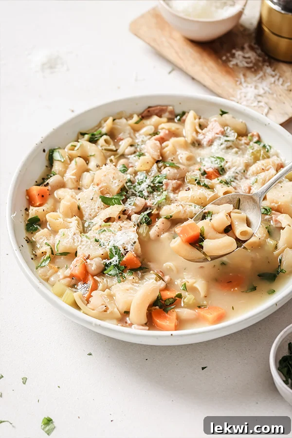 A bowl of white pasta fagioli soup with a spoon taking a spoonful of soup out.