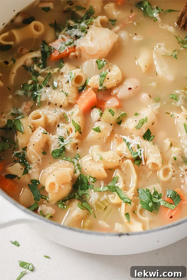 White pasta fagioli soup in a white dutch oven topped with chopped parsley.