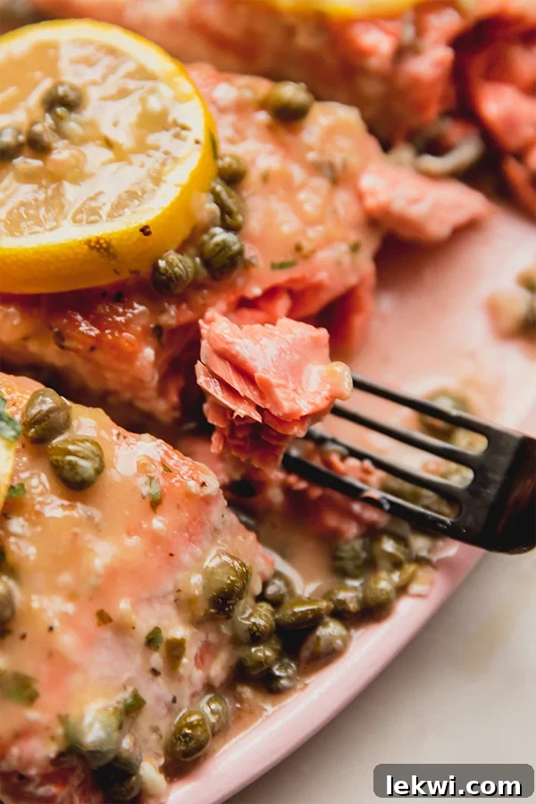 A fork lifts a succulent bite of salmon piccata from a beautifully presented serving platter, garnished with lemon and capers.