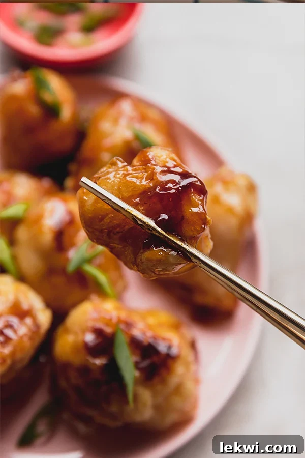A set of wooden chopsticks picking up a perfectly glazed teriyaki crispy cauliflower wing.