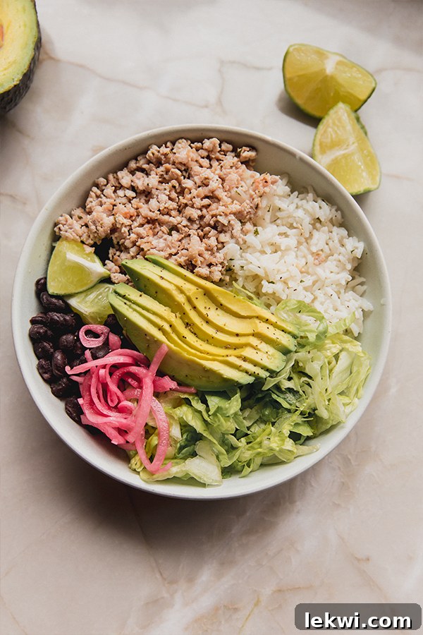 A vibrant bowl filled with seasoned ground chicken, fluffy lime cilantro rice, black beans, creamy avocado slices, and fresh shredded romaine lettuce.