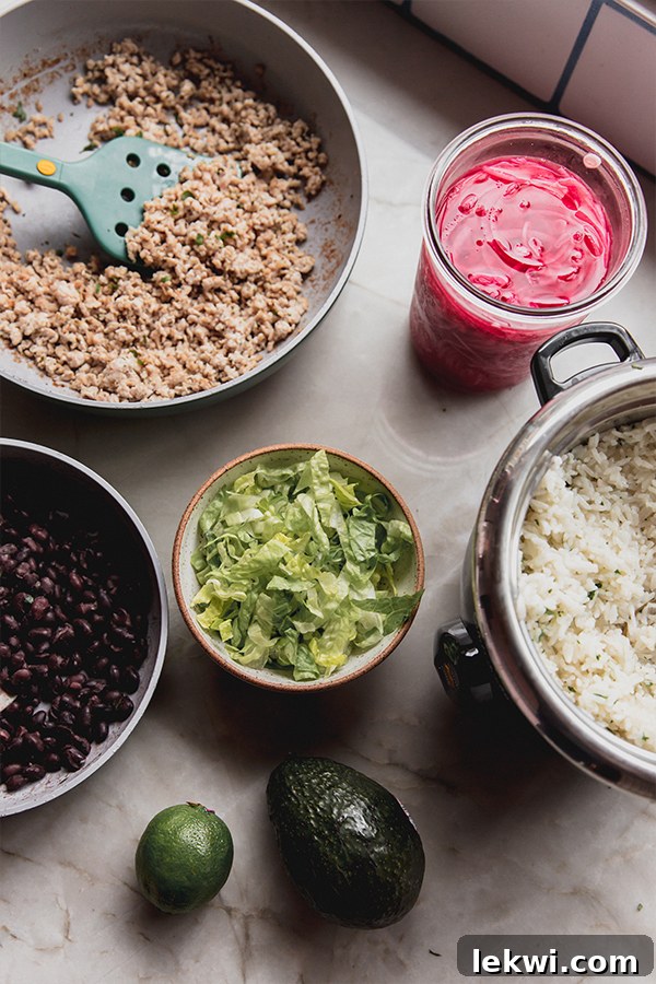 All the fresh ingredients laid out on a kitchen counter, including ground chicken, various spices, rice, limes, avocados, and fresh herbs, ready for assembling the chipotle-style bowls.