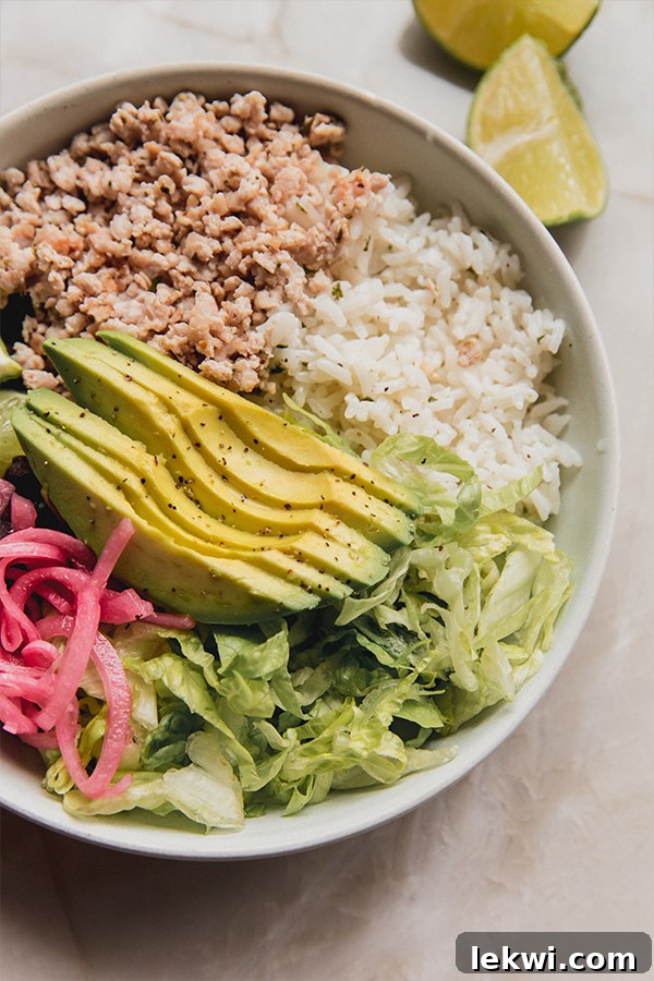 A close-up shot of a perfectly assembled ground chicken chipotle style bowl, showcasing the rich colors of the chicken, rice, beans, avocado, and pickled onions, ready to be enjoyed.