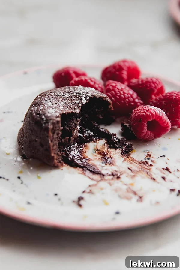 Partially-eaten lava cake on a plate with raspberries.