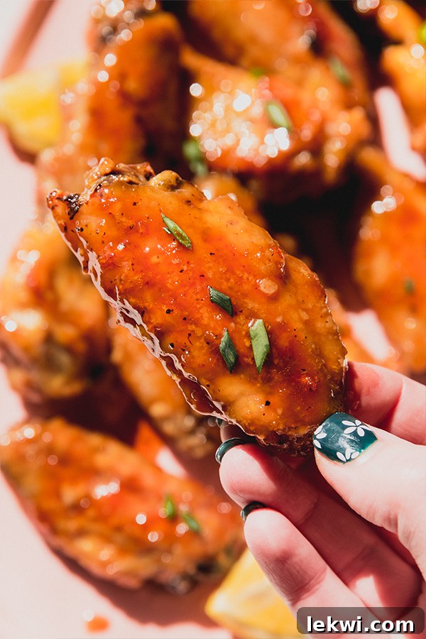 A perfectly glazed lemon garlic chicken wing being held up, with a platter of more wings blurred in the background, ready to be enjoyed.