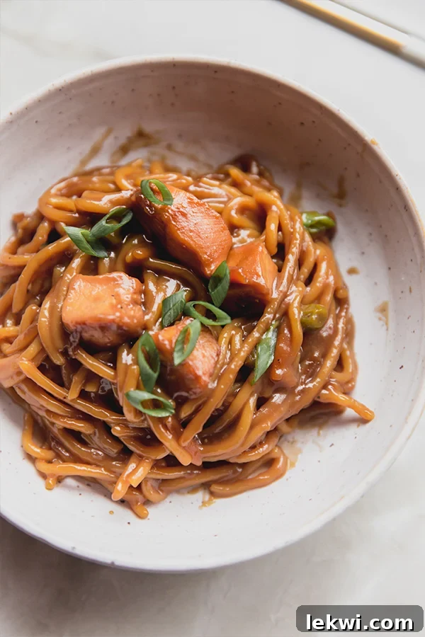 A close-up shot of a single serving of baked honey garlic chicken noodles in a bowl, garnished with fresh green onions, ready to be enjoyed.