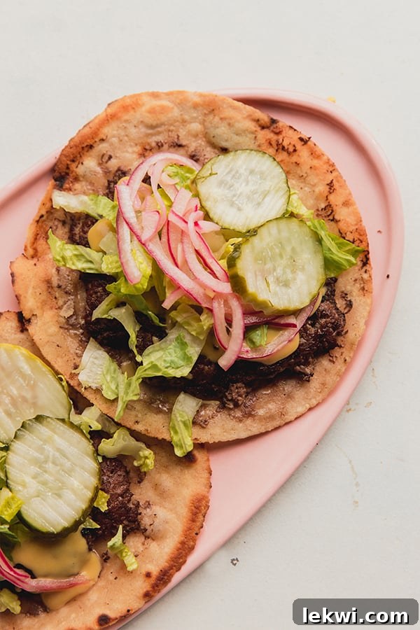 A serving plate with two smash burger tacos topped with pickled onions and pickles.