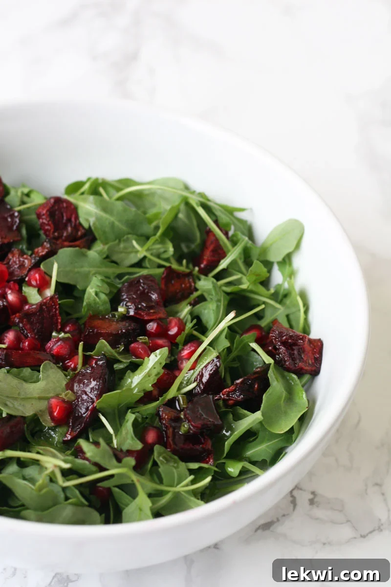 Arugula salad in a white bowl with pomegranate seeds and roasted beets, showcasing a delightful Pomegranate Beet Fall Salad.