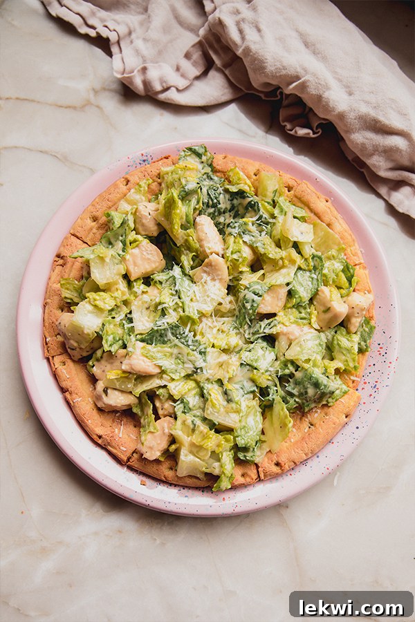 Close-up shot of a plate of chicken Caesar salad pizza, showcasing its fresh ingredients.