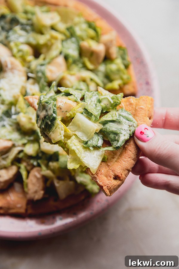 A hand reaching for a piece of Chicken Caesar Salad Pizza on a wooden board.