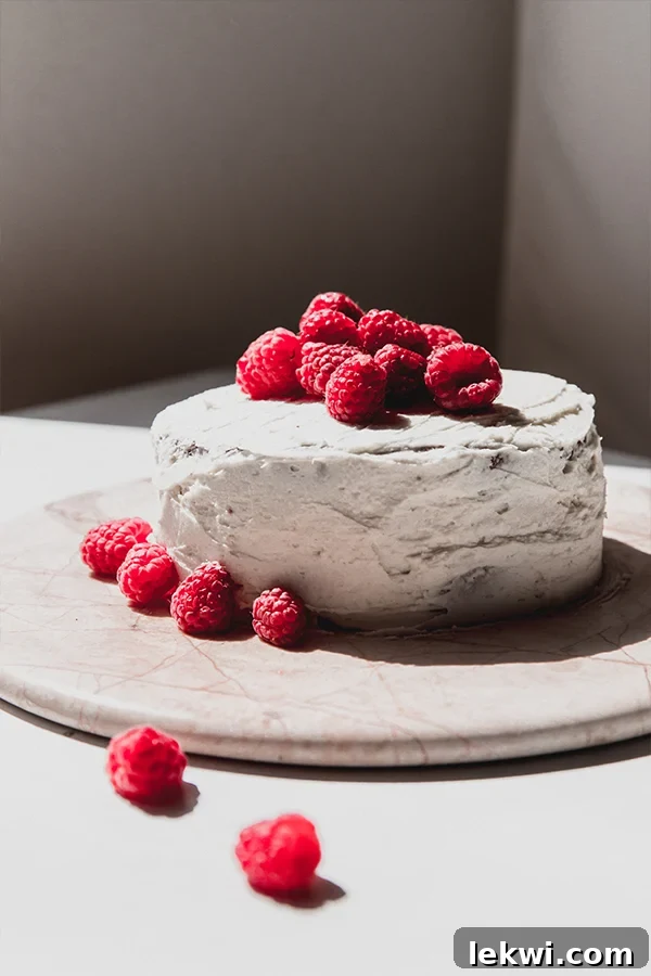 An exquisite gluten-free white chocolate raspberry cake, beautifully iced and generously topped with fresh, glistening raspberries, ready for serving.