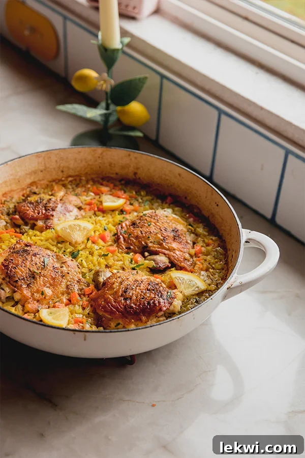 Greek lemon chicken thighs in a large white pan with rice, diced carrots, lemon wedges, and topped with parsley.