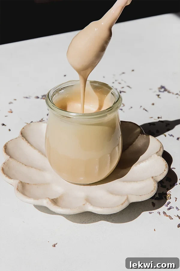 Whipped honey in a small glass jar sitting on a plate, with a spoon dipping in to show a drizzle of honey.