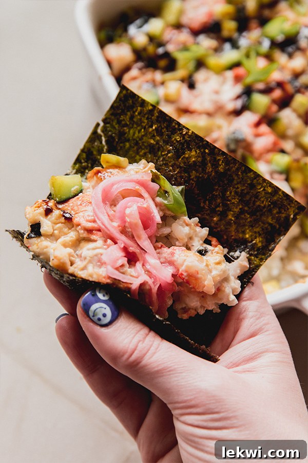 A piece of seaweed wrapped around the mini sushi bake topped with pickled onions.