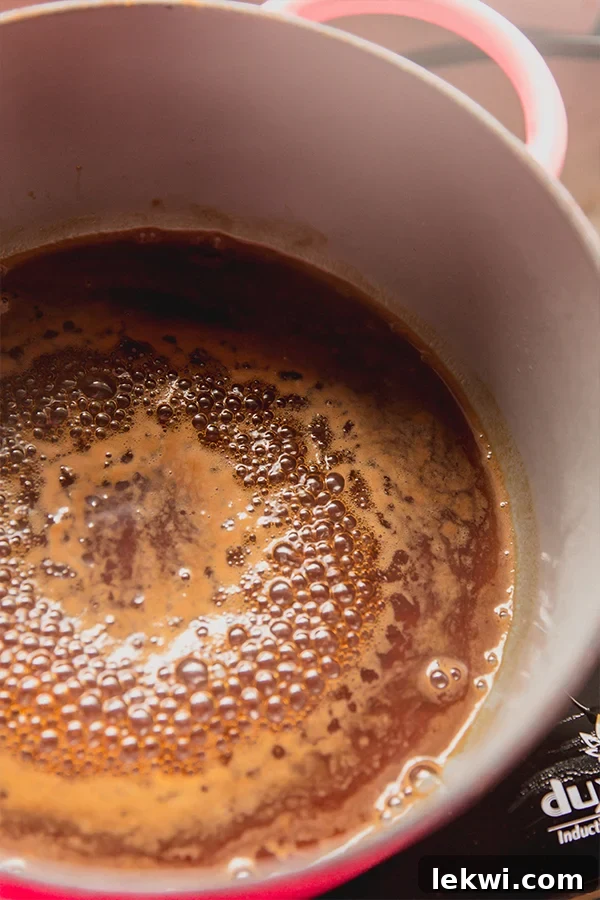 A small pot gently simmering with homemade almond simple syrup on a stovetop, indicating the first step of preparation.