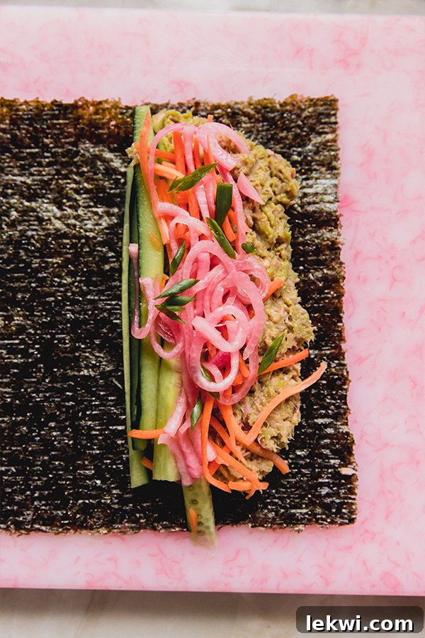 A perfectly assembled tuna salad seaweed wrap, laid flat on a surface before being rolled, showcasing all the fresh ingredients like tuna, cucumber, carrot, pickled onion, and green onion.