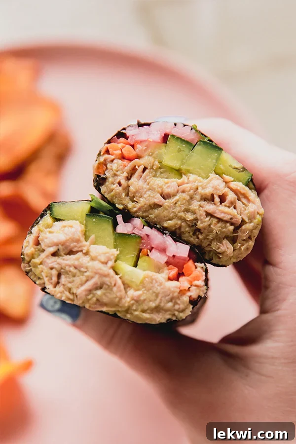 Tuna salad roll up cut in half to show the cucumber, carrot, pickled onion and tuna, being held with a hand.