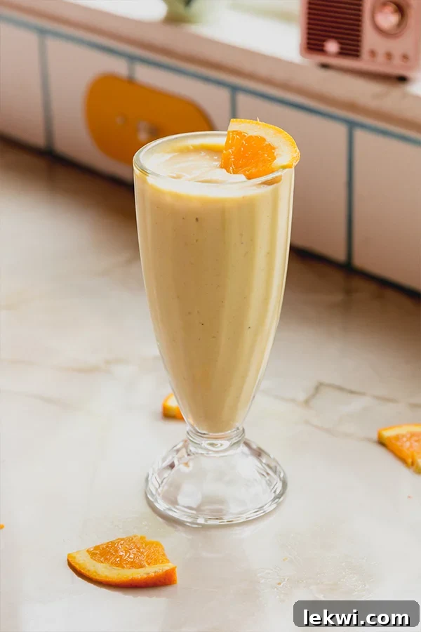 A perfectly blended dairy-free creamsicle frosty in a tall glass, garnished with a vibrant orange slice, showcasing its vibrant color and creamy texture.