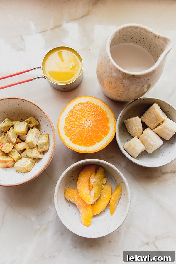 Fresh, whole-food ingredients laid out on a countertop, ready to be blended into a homemade creamsicle frosty, including frozen fruit, coconut milk, and orange segments.