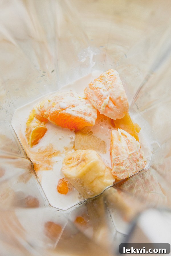 All ingredients for the creamsicle frosty, including frozen banana, peach, Japanese sweet potato, and orange juice, loaded into a high-speed blender, ready for mixing.