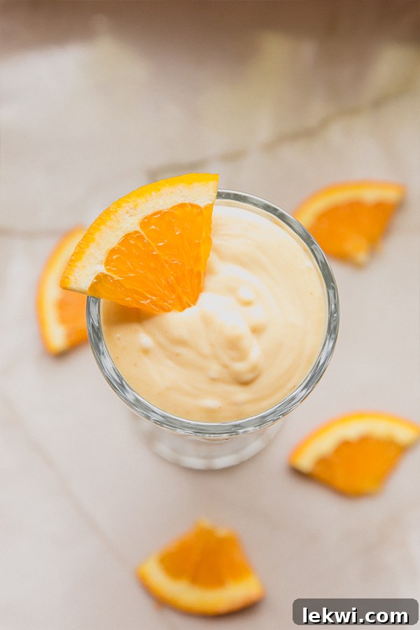 An inviting overhead view of two dairy-free creamsicle frosties in glasses, topped with fresh orange slices, against a light background, emphasizing their creamy texture.