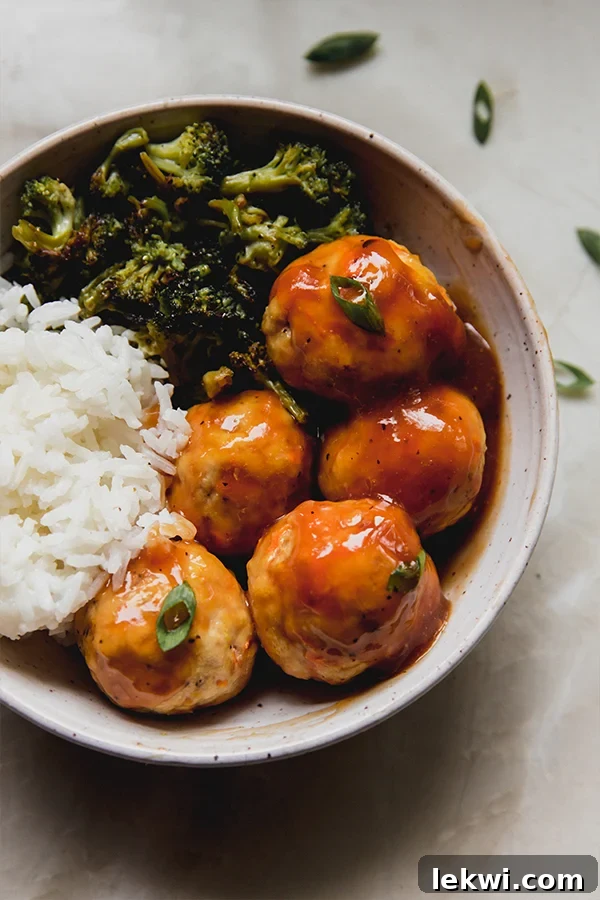Sweet and sour chicken meatballs topped with green onion in a bowl with white rice and broccoli, ready to be served.
