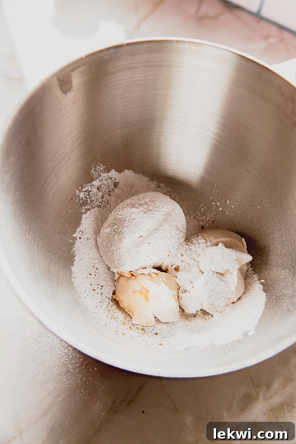 A stand mixer bowl filled with unmixed dairy-free cream cheese, coconut whipped cream, and powdered sugar, ready to be whipped into a smooth, fluffy consistency.