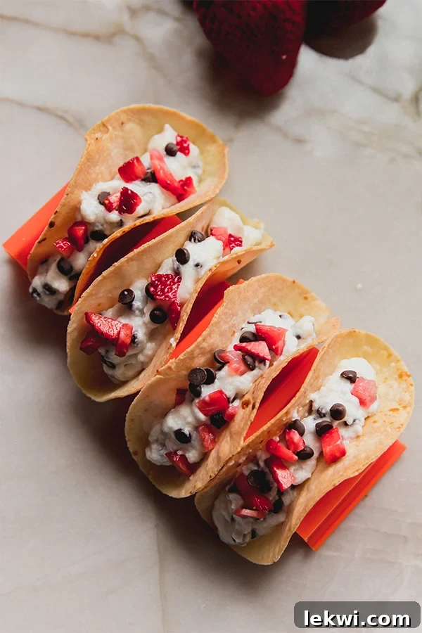 Cannoli tacos topped with strawberries and chocolate chips in a taco holder.