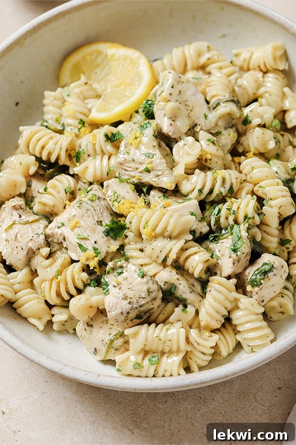 Lemon chicken pasta bake in a large white bowl, topped with parsley and lemon slices.