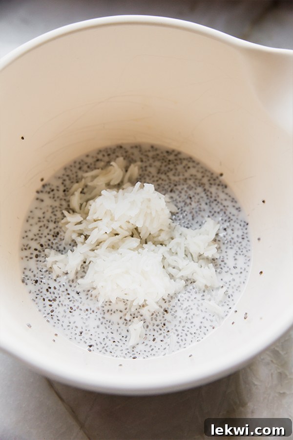 A close-up shot of a bowl of mango sticky rice chia pudding being mixed with a spoon, showing the creamy texture infused with basmati rice grains.