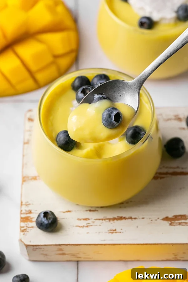 A single cup of dairy-free mango pudding with a spoon scooping out a bite, showcasing its creamy texture.