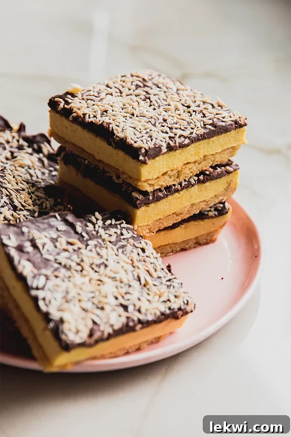 Lemon smores bars topped with toasted coconut, stacked on a pink plate.